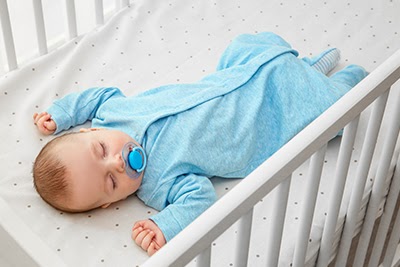 Baby in blue pajamas sleeping with pacifier in his mouth
