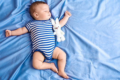 Baby boy sleeping on his back with plush bunny by his side