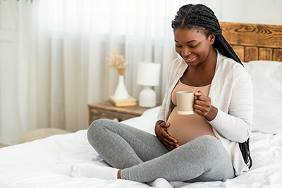 pregnant woman holding a coffee cup in bed