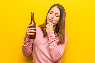 Young cute woman holding a beer doubting