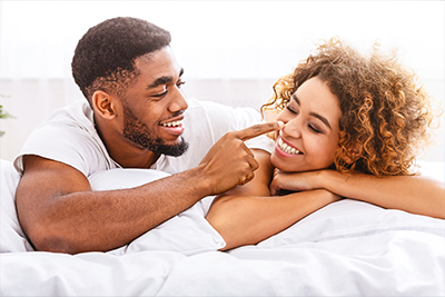 Playful african man flirting with wife, touching her nose in bed